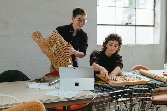 two women creating art together, one cutting into a netmaterial while the other one watches