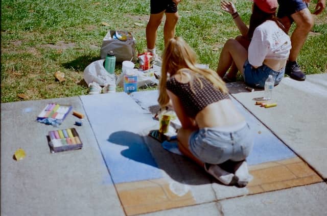Girl drrawing with coloured chalk on the ground while hanging out with her friends
