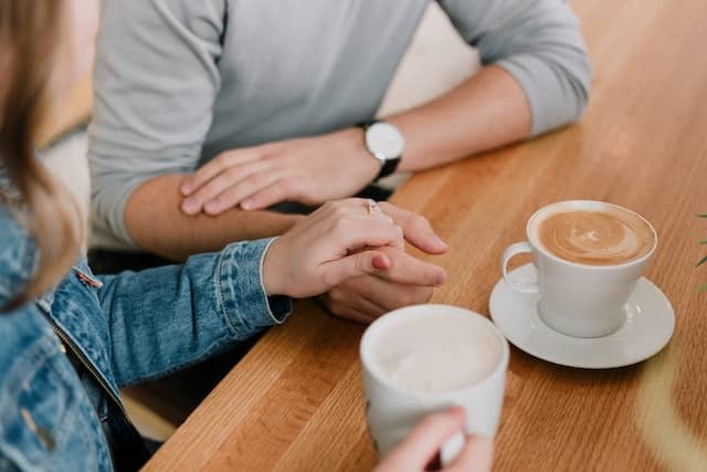 a couple sitting down at a table, holding hands and having coffee