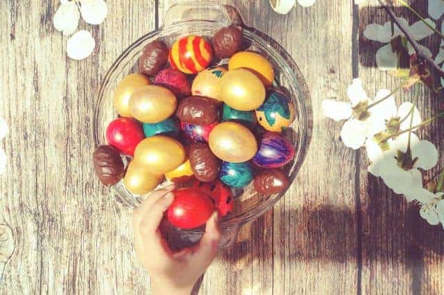 brightly decorated easter eggs in a bowl on a wooden table outside
