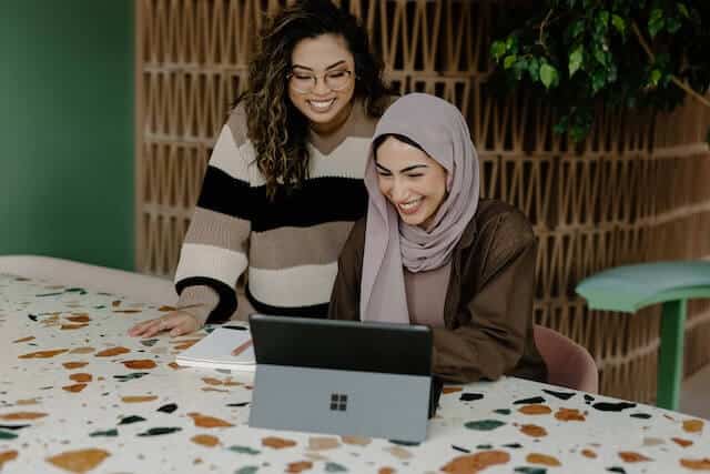 two women of ethnic minority smiling and looking at a computer screen