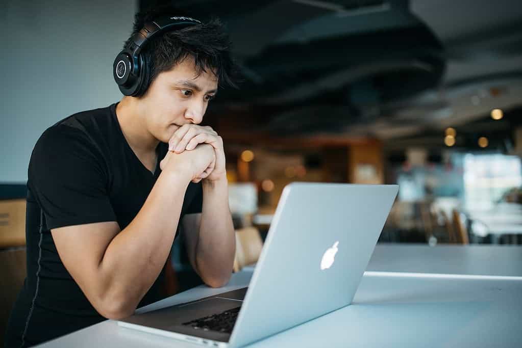 man sitting at desk with headphone on and looking at his laptop