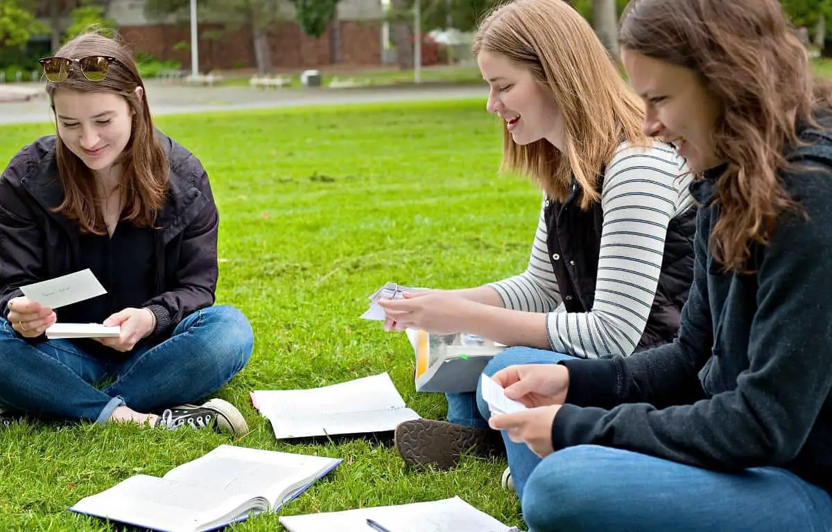 3 female students sitting on grass and using flashcards to active recall the study material