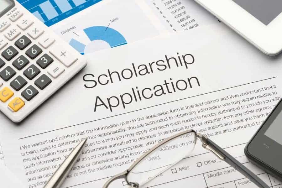 scholarship application written on form on desk with glasses, pen and calculator on tabletop