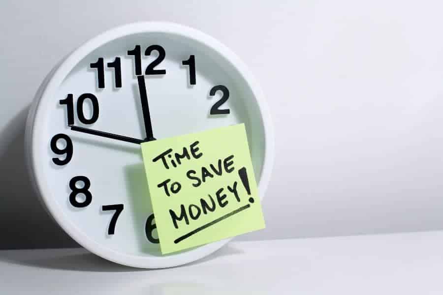 white clock on desk with yellow post it note with time to save money written on it