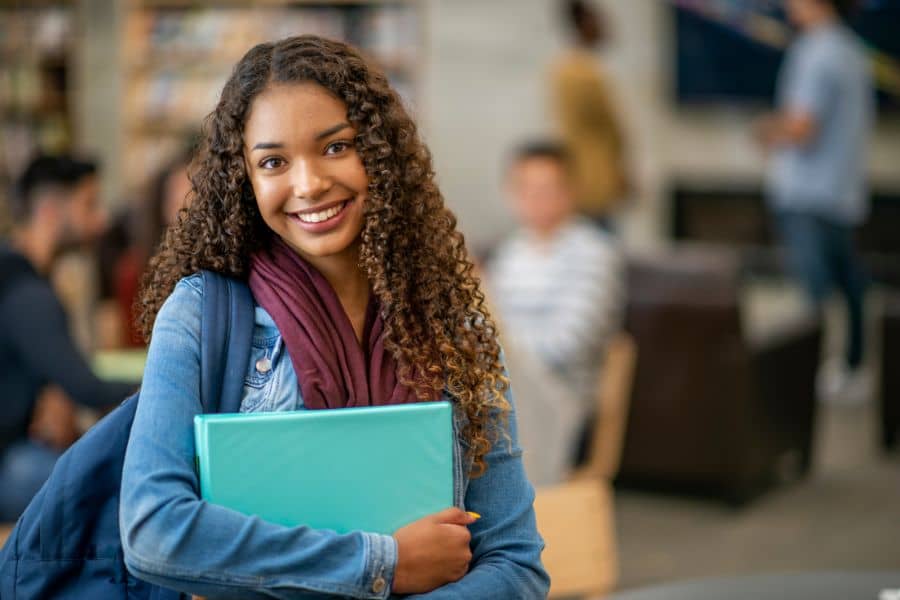female student standing and holding a blue folder in her arms wondering how to be popular in college