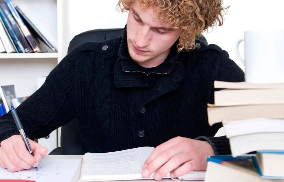 male college student sitting at desk and taking notes from a textbook