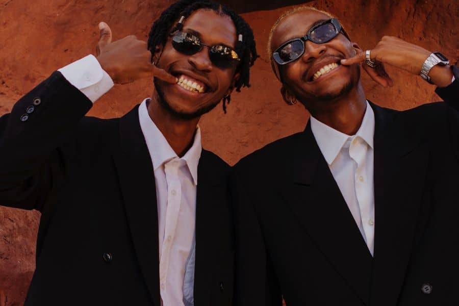 two black men posing in black suits and wearing sunglasses