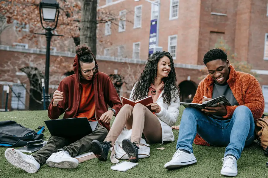 three college students sitting on campus with their laptop and books
