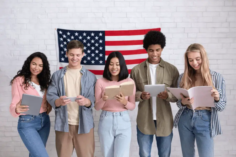 group of students standing and holding books and tablet in their hands with an usa flag behind them