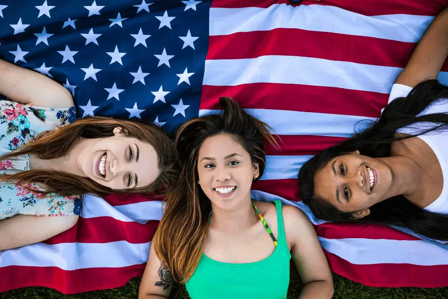 female students laying on the usa flag on the grass