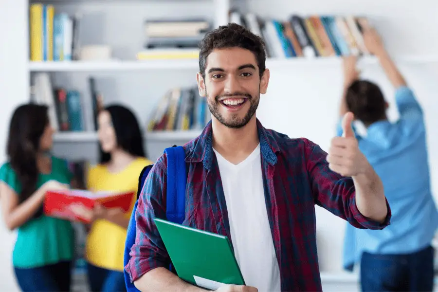 male student holding books and giving the thumbs up with a smile