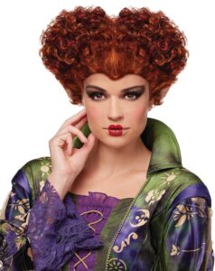 Image of a woman wearing an elaborate curly red wig styled in a heart-shaped updo, with bold makeup and a detailed green and purple costume. This dramatic and enchanting look is ideal for **halloween costumes red hair**, perfect for portraying a classic witch or fantasy-inspired villain.